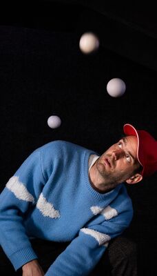 Een man kijkt omhoog naar drie bewegende witte ballen in een donkere ruimte.