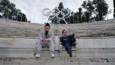 Twee mensen zitten op een verlaten tribune. Het Olympisch logo staat achter hen.