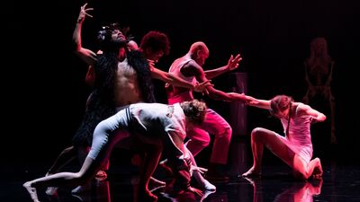 Vijf dansers op een podium, in rood licht uitgelicht.