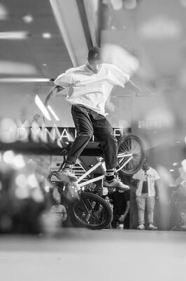 Een persoon met een wit shirt en een pet doet een truc op een bmx fiets.