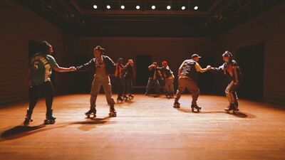 Een groep van acht mensen op rolschaatsen, verdeeld in duo's die ekaars hand vasthouden.