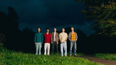 Een bandfoto van 5 mensen.